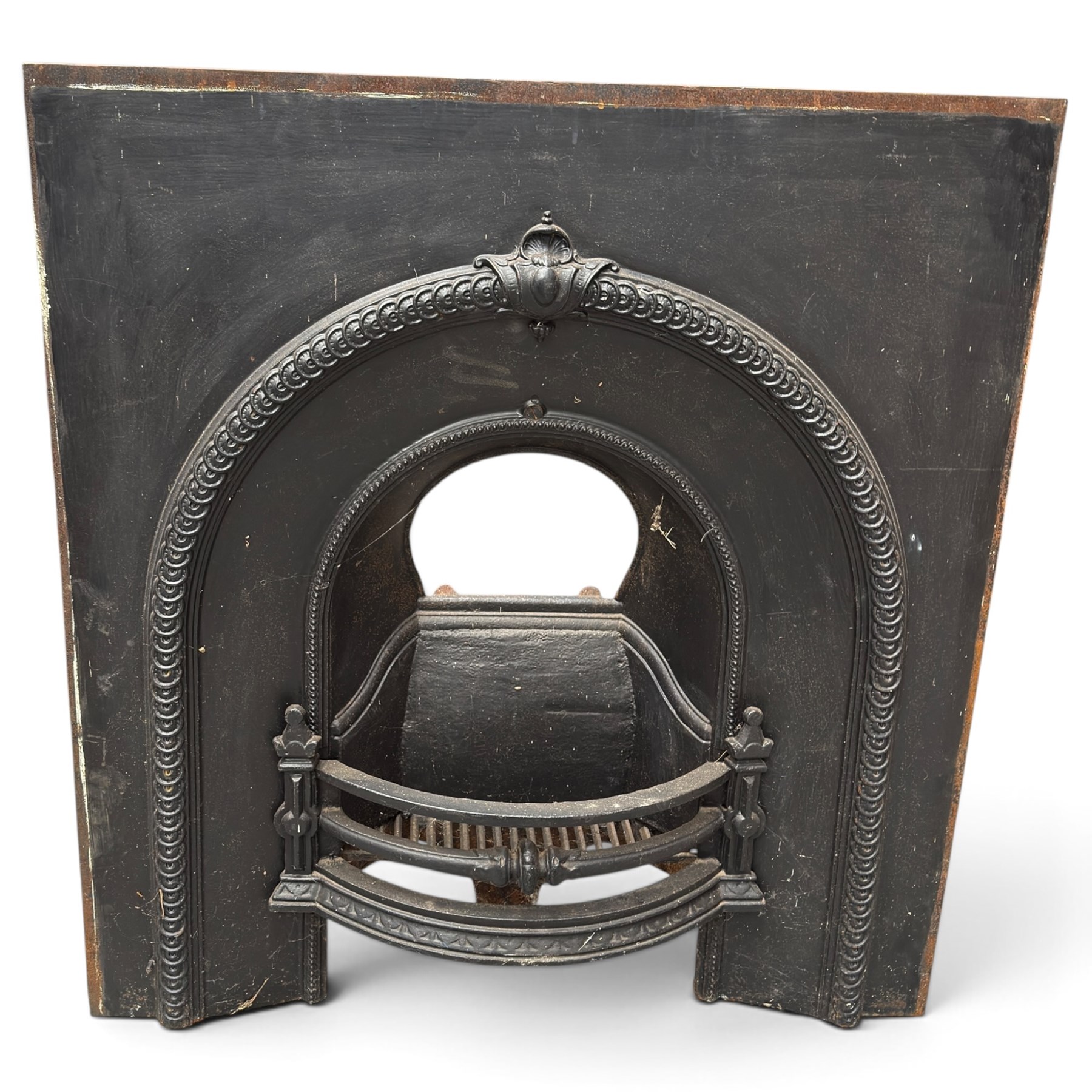 Late Victorian black-painted cast iron fireplace, the arched surround with anthemion cartouche and guilloche-moulded border, enclosing a bow-front fire basket with finialled standards, railed front and leaf-cast apron, with sheet-metal backplate
