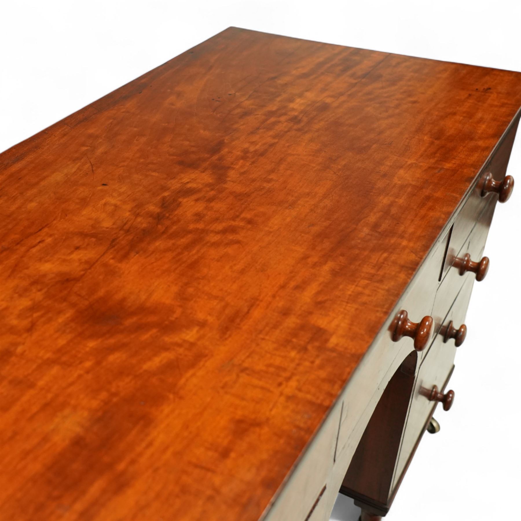 Early 19th century mahogany kneehole desk, rectangular moulded top over an arrangement of nine drawers with turned mahogany handles, arched kneehole recess, raised on short turned legs with brass cups and castors