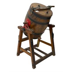 19th century oak and cast iron rotary butter churn, with coopered barrel body, domed lid with filler opening and cast iron securing arms, on tilting iron-mounted frame with crank handle and support rails