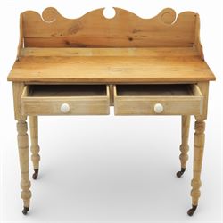 19th century stripped pine side table, the rectangular plank top with low shaped back rail incorporating scroll cut ends, fitted with two frieze drawers with ceramic knob handles, raised on turned supports terminating in castors