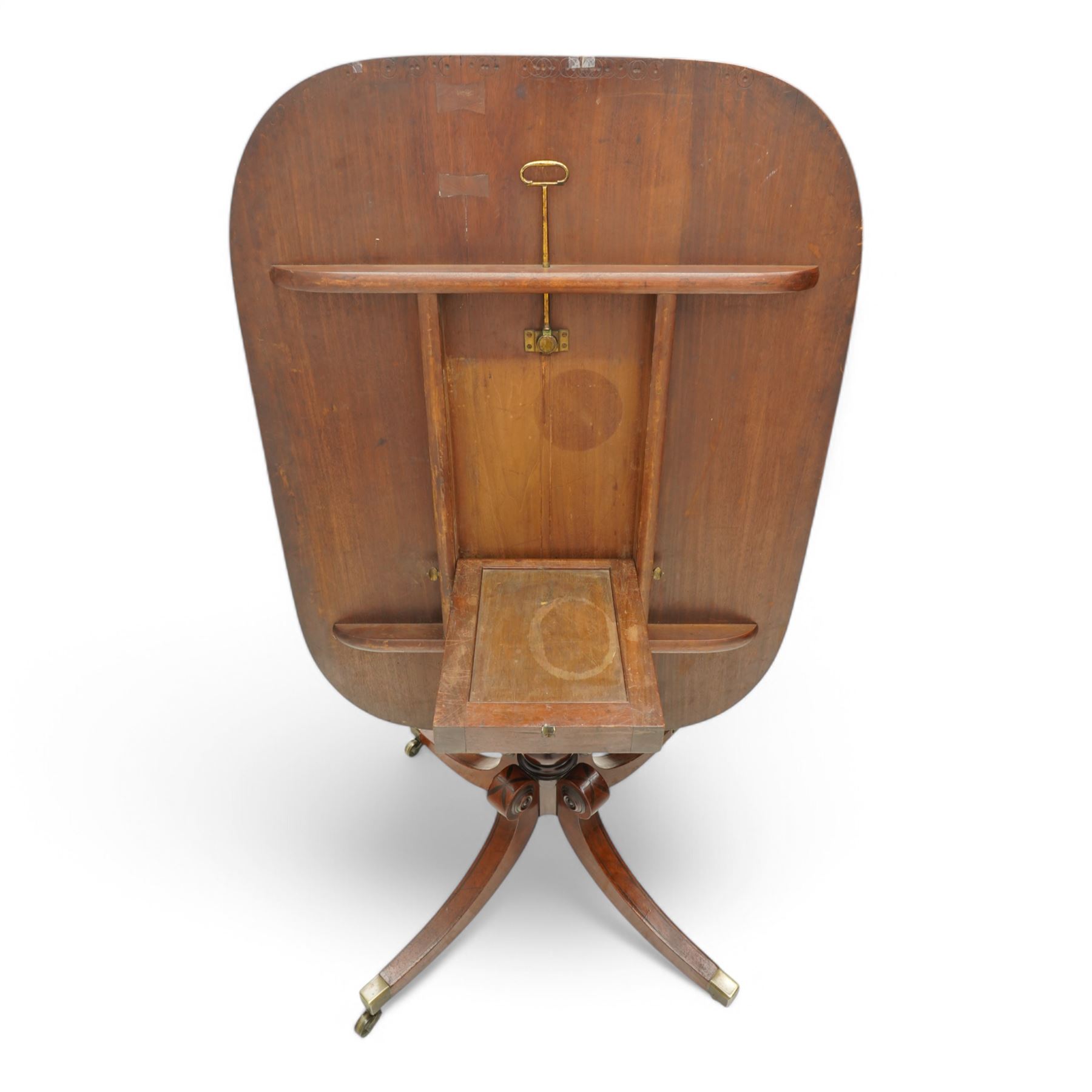 Regency figured mahogany breakfast table, figured rectangular tilt-top with rounded corners and rosewood banding, on turned column with four out-splayed supports with brass cups and castors 