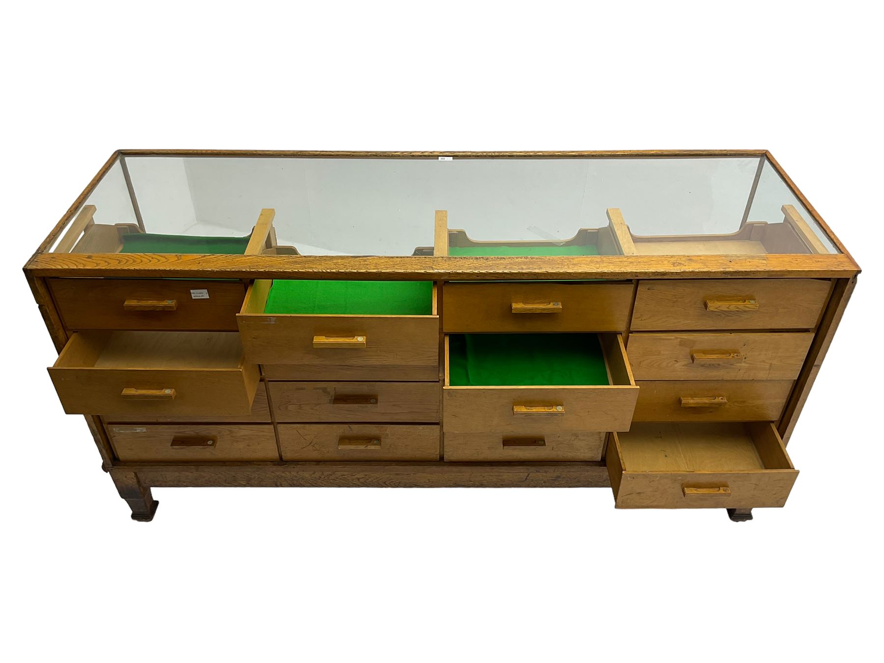 Early 20th century oak framed haberdashery shop counter, glass panel exterior enclosing sixteen graduating drawers with oak fronts and handles, raised on shaped tapering supports 
