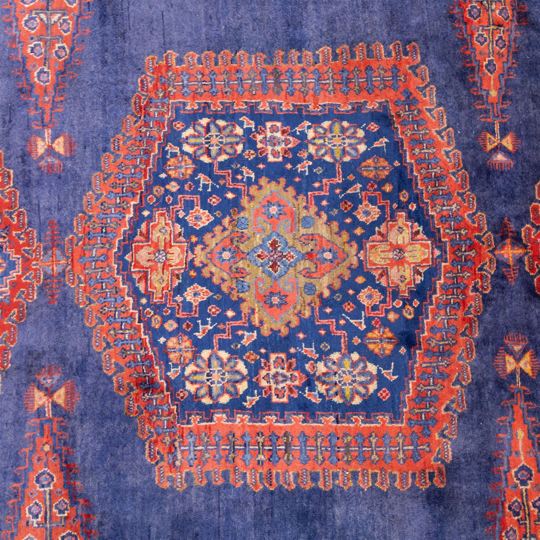 Central Persian Veis hand-knotted carpet, deep blue indigo field with central stepped lozenge medallion filled with stylized floral and geometric motifs, flanked by further angular medallions and tribal devices, edges with articulated and serrated hooked forms within a wide geometric border with repeating stylized floral motifs and multiple guard borders, in madder red, indigo blue, ivory, olive green, with cotton fringe ends