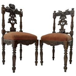 Pair of 19th century heavily carved oak side chairs, cresting rail with carved Putti mask over pierced and carved splat with ornithological decoration, sprung seat upholstered in red fabric over foliate and scroll carved frieze, on turned supports