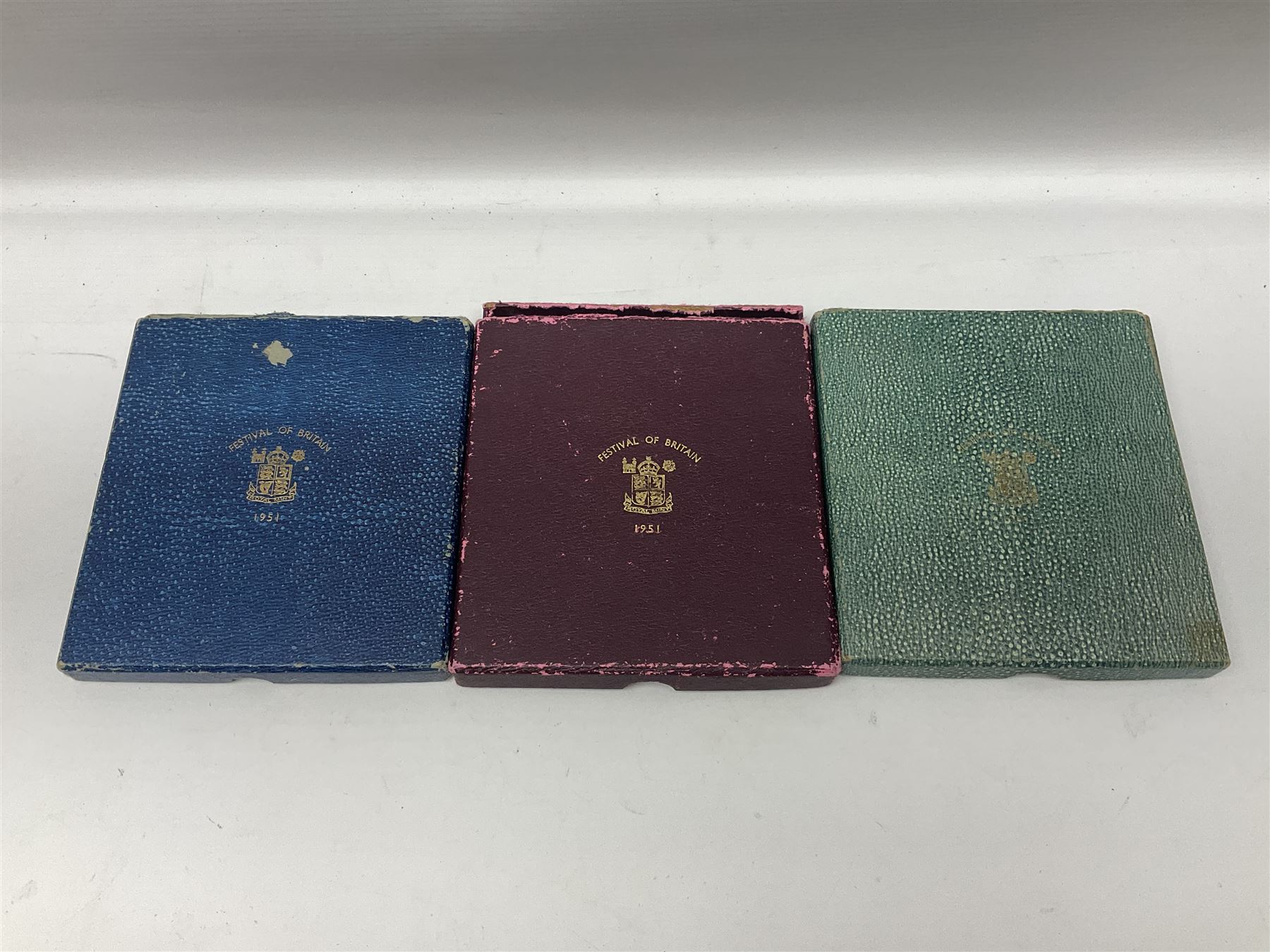 Three King George VI 1951 'Festival Of Britain' specimen coin sets, each comprising farthing to crown coins, housed in maroon, green and blue dated boxes 