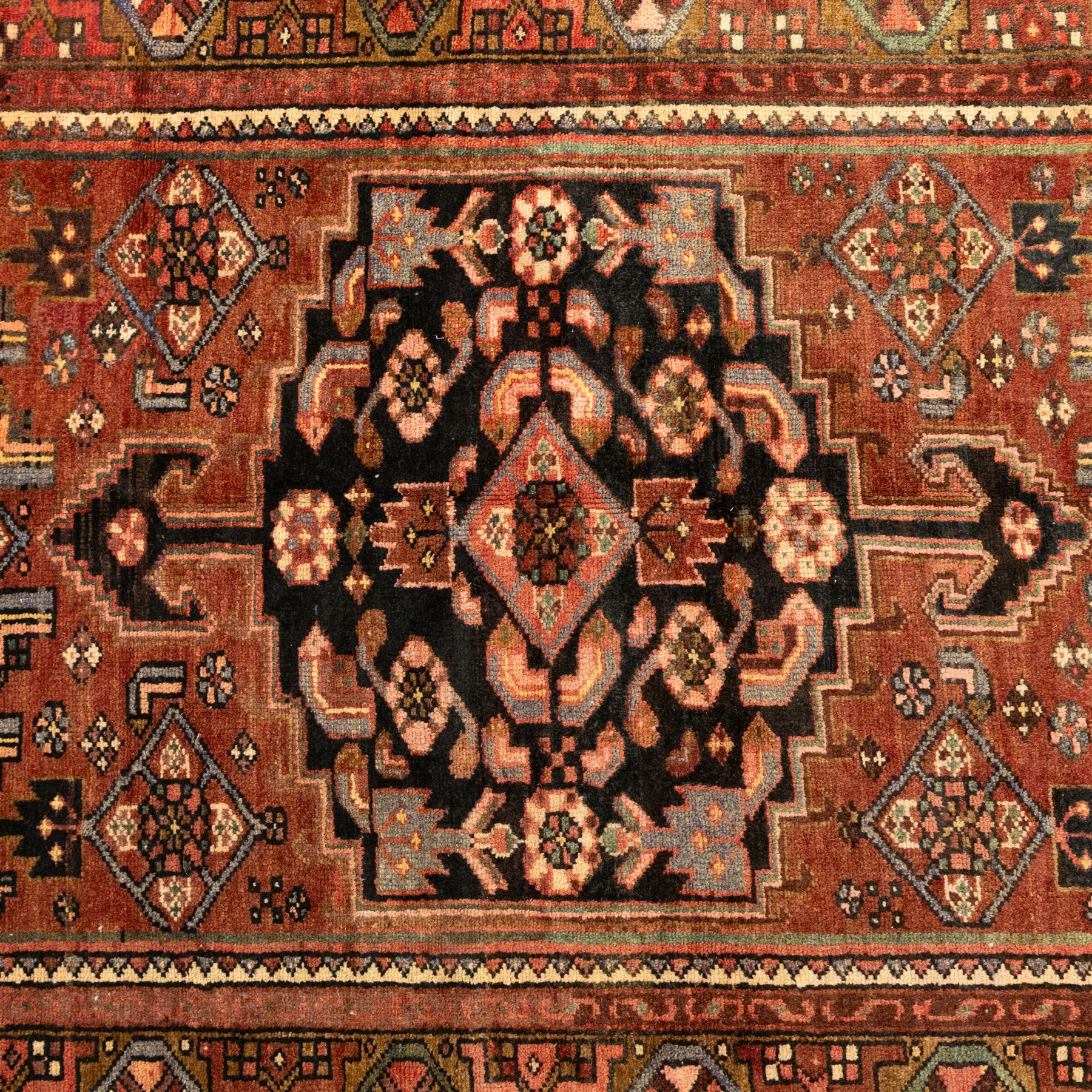 North West Persian Zanjan hand-knotted rug, madder-red field with a central stepped lozenge medallion enclosing stylized geometric floral motifs in indigo, ivory, and brown, angular spandrels filled with tribal devices and framed by a series of geometric borders with latch-hook rosette and leaf motifs, with cotton fringe ends  