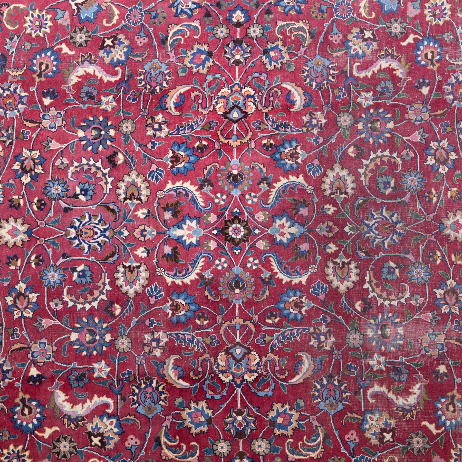 Persian Mashad design wool carpet, the red ground with dense scrolling floral and foliate decoration, within dark blue main border decorated with repeating palmettes and shaped leaves