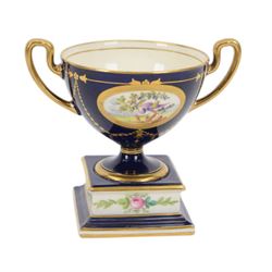 Early 20th century Minton porcelain twin handled pedestal cup, decorated with two reserve painted with birds against a blue ground, upon a square plinth painted with pink roses, the whole heighted with gilt, with puce printed mark beneath, H11.5cm, together with an early 20th century Minton twin handled vase, of ovoid form decorated with two painted portrait medallions, surrounded by gilt foliate scrolls, upon a blue ground, the neck painted with a band of pink roses, with gilt printed mark beneath, H11.5cm, and an early 20th century Minton twin handled pedestal vase and cover, painted with pink rose and vine swags upon a white ground, with puce printed mark beneath, H18.5cm, (3) 