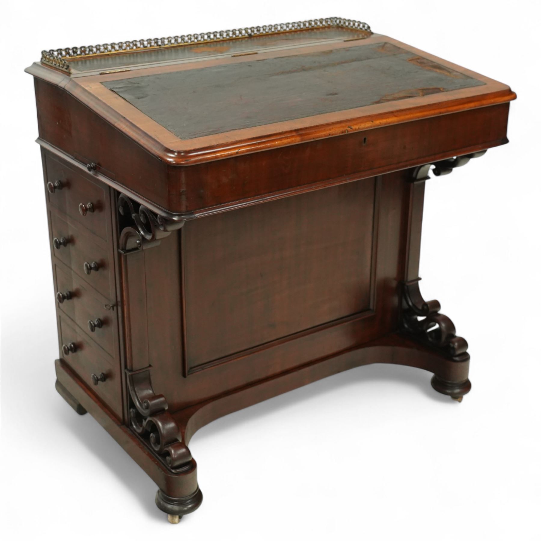 Large Victorian mahogany Davenport, the sloped leather inset writing surface opening to reveal fitted interior, with four drawers to one side and opposing dummy front cupboard door, carved scrolled supports and panelled back, raised on turned feet with brass castors 