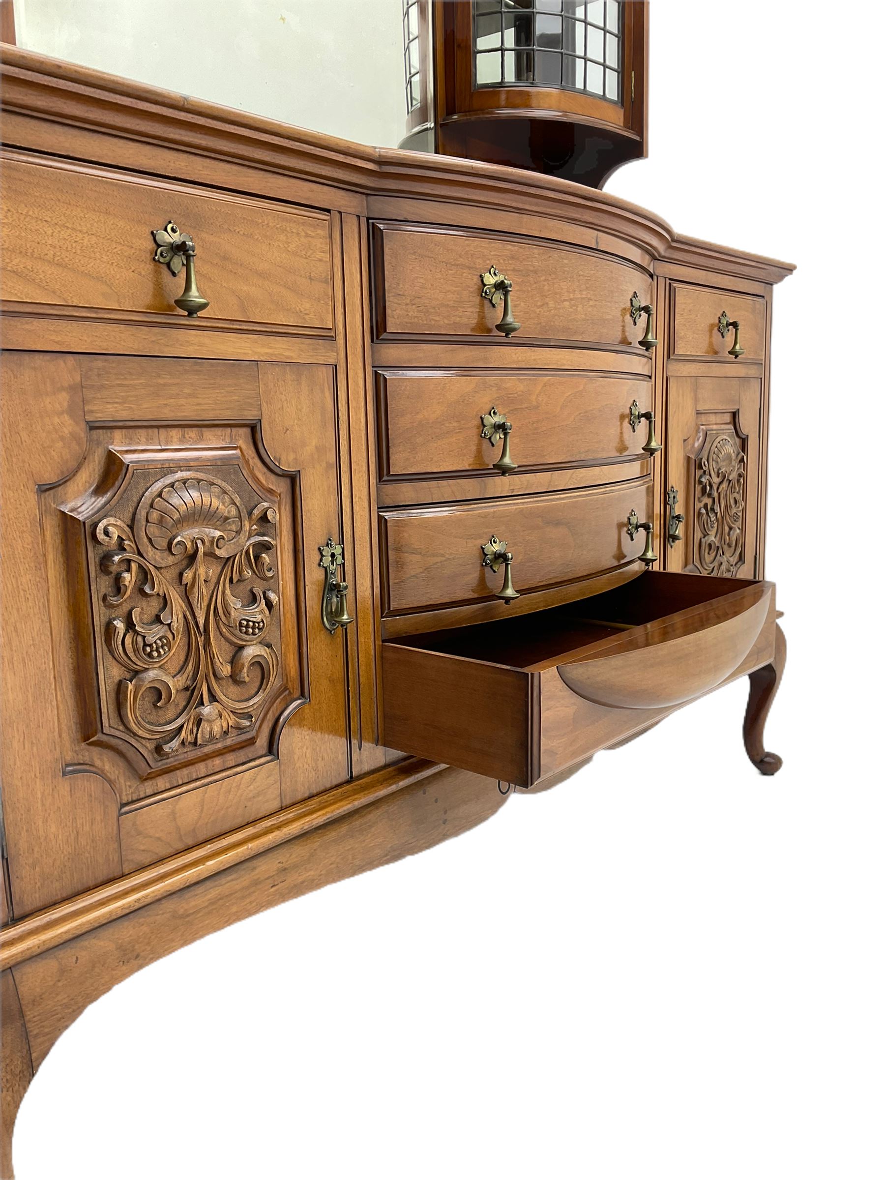 Late Victorian walnut mirror back sideboard or dresser, the raised back fitted with two curved and lead glazed cabinets, central arched bevelled mirror, the sideboard with break bowfront, fitted with six drawers and two cupboards, the cupboard doors panelled and carved with scrolls, shell and plant motifs, shaped apron with cabriole feet
