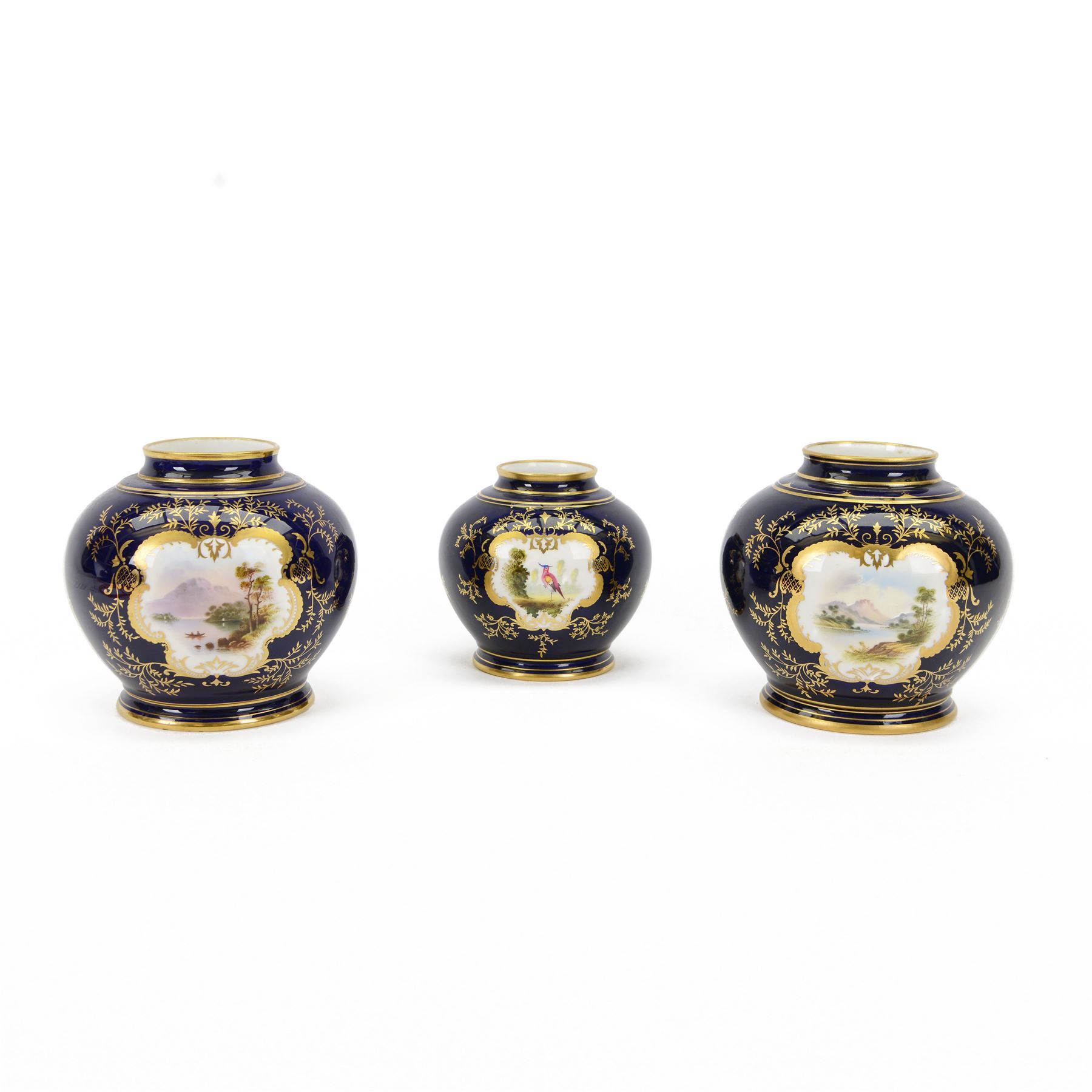 Pair of early 20th century Coalport vases, each of squat bulbous form, decorated with hand painted reserves of landscapes against a blue ground heightened with gilt, with printed marks beneath and numbered V5146 in gilt, H13cm, and a similar smaller example painted with a reserve of an exotic bird, numbered 5146, H11cm