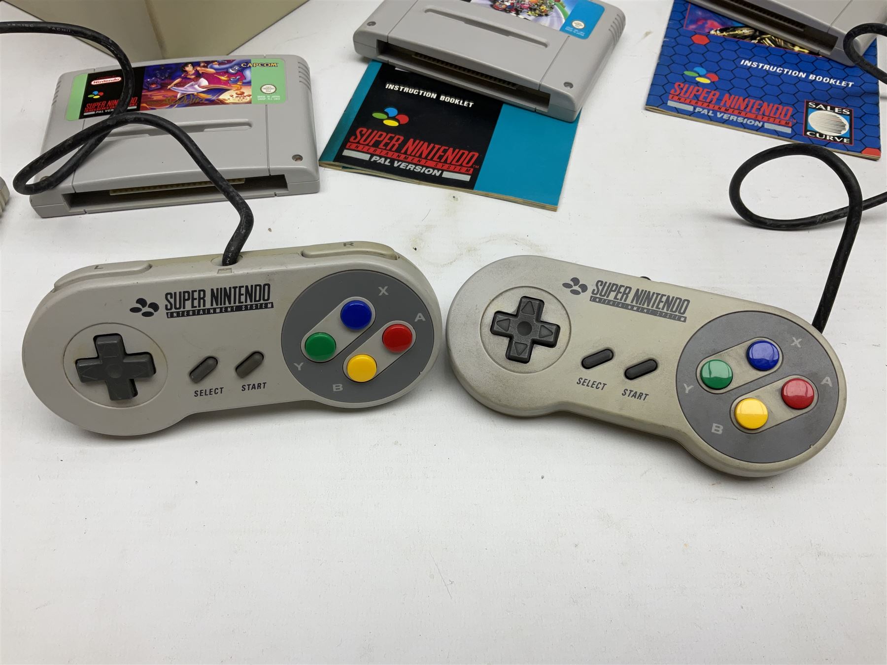 Two Super Nintendo Entertainment System (PAL) controllers, accessories and games. Super NES Game Commander with original box and instruction booklet, Super NES Nintendo Scope (1992) transmitter gun, receiver, Super NES Nintendo Scope 6 game with original instruction booklets. Further games to include ‘The Legend of Zelda a Link to the Past’, ‘Super Mario World’, ‘Super Mario Kart’, ‘The Lawnmower Man’, and ‘Exhaust Heat’, all with original instruction booklets. ‘PowerMonger’ and Disney’s ‘Aladdin’ game cartridges only 
