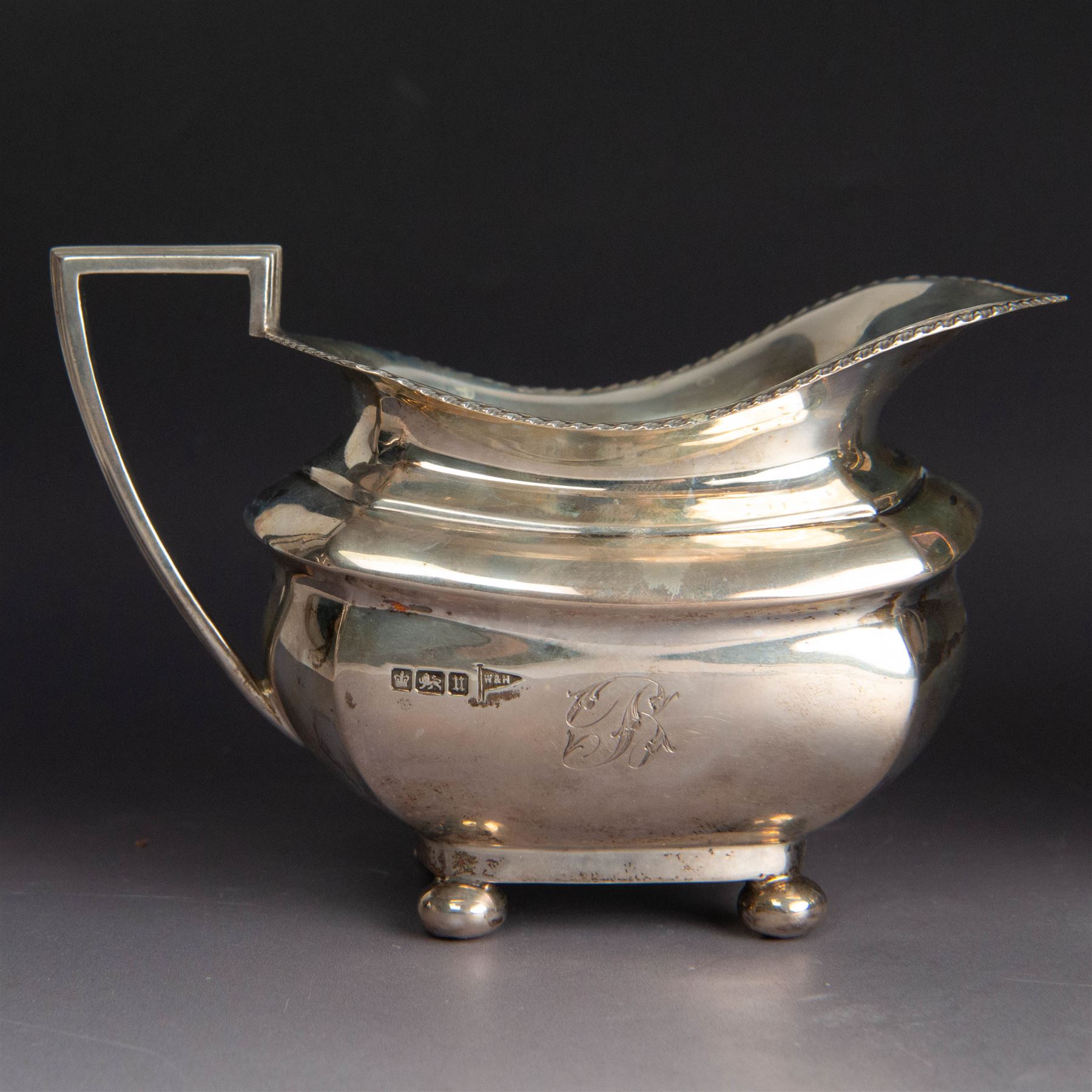 Early 20th century three piece silver tea service, comprising teapot, open sucrier and milk jug, all with oblique gadrooned rim, engraved initial to body and upon four bun feet, the teapot with Bakelite type handle and finial, hallmarked Walker & Hall, Sheffield 1912, contained within an oak presentation case with silk lining