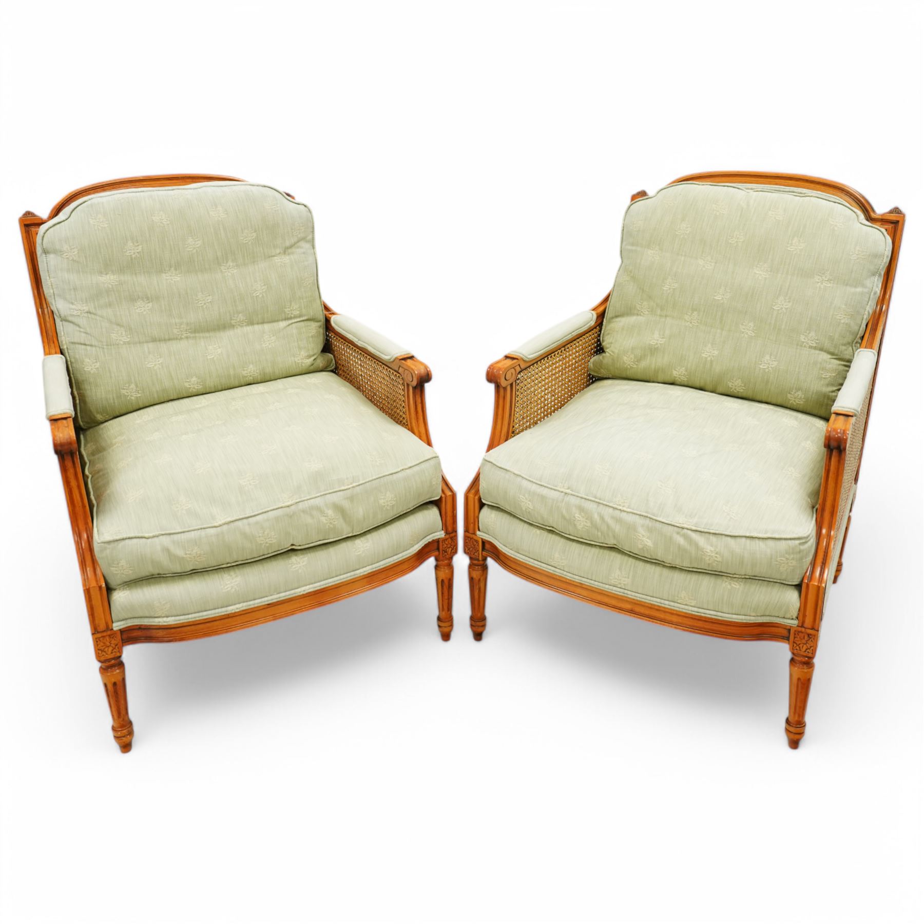 French Empire design varnished wood three piece lounge suite comprising of two cane armchairs and matching sofa, carved top rails with foliate terminals, cane side panels and padded scroll arms, upholstered in a green brocade with matching piping, on fluted legs