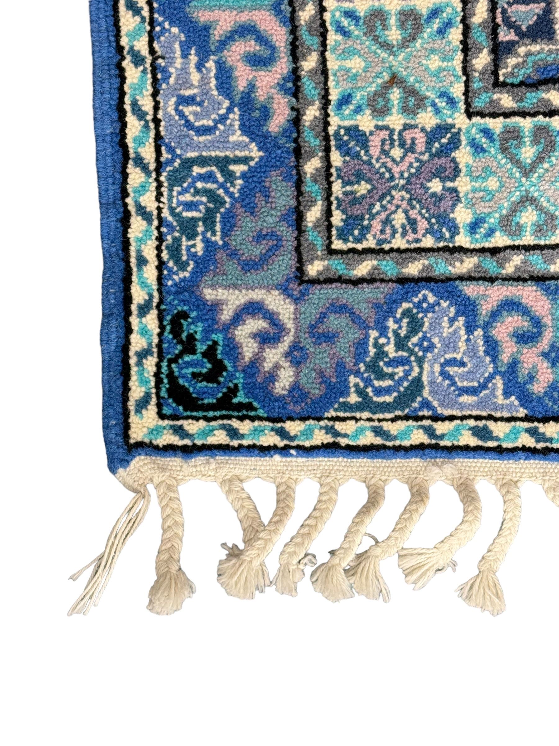 Morrocan single weft blue ground rug, the field segmented into a grid of ten rectangular panels, bordered by a series of guard bands with repeating floral and geometric patterns with interlocking vines and rosettes, the edges finished with a fringe of twisted tassles