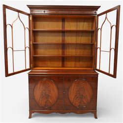 William Tillman - Early 20th century mahogany display cabinet, moulded cornice above a frieze carved with roundels and fluting, pair of astragal glazed doors enclosing adjustable shelving, the lower section fitted with twin panelled cupboard doors centred with oval veneered panels, shaped apron and bracket feet