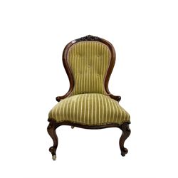 Victorian mahogany framed nursing chair, cresting rail carved with foliate cartouche, upholstered in buttoned striped fabric with sprung seat, raised on cabriole supports terminating in ceramic castors