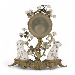 French- early 20th century 8-day Chinoiserie brass and porcelain mantel clock in the 18th century style, brass base with splayed feet profusely decorated with clusters of painted porcelain flowers and two decoratively painted Chinese foo dogs, movement enclosed in a circular porcelain movement case illustrated with birds of paradise and oriental motifs, with a white enamel dial Arabic numerals, minute markers, pierced gilt hands and a floral swag, rack striking Parisian movement striking the hours and half-hours on a bell. With a visible sunburst pendulum and key.