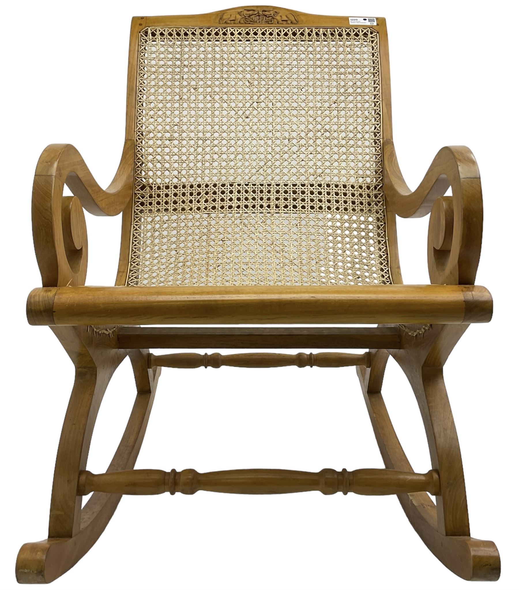 Late 20th century teak framed plantation style rocking chair, cresting rail carved with two elephants with upraised trunks, cane back and seat with scrolled arm terminals, rocker base united by turned stretcher