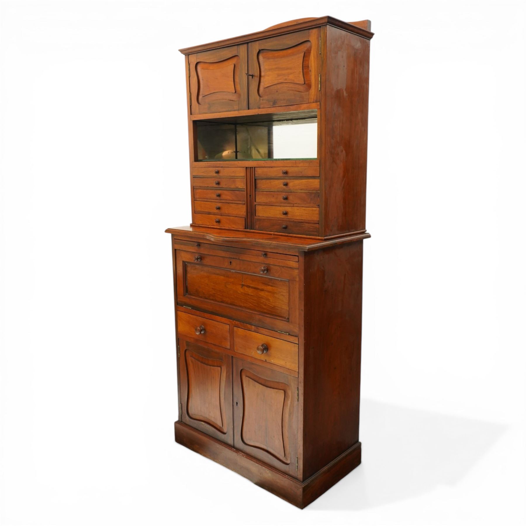 19th century walnut dentist cabinet, galleried top above twin cupboard doors with mirrored interior, recessed mirrored section, two banks of five graduated drawers, shaped section with brushing slide above a fall front, two short drawers and twin cupboard doors, on a plinth base 