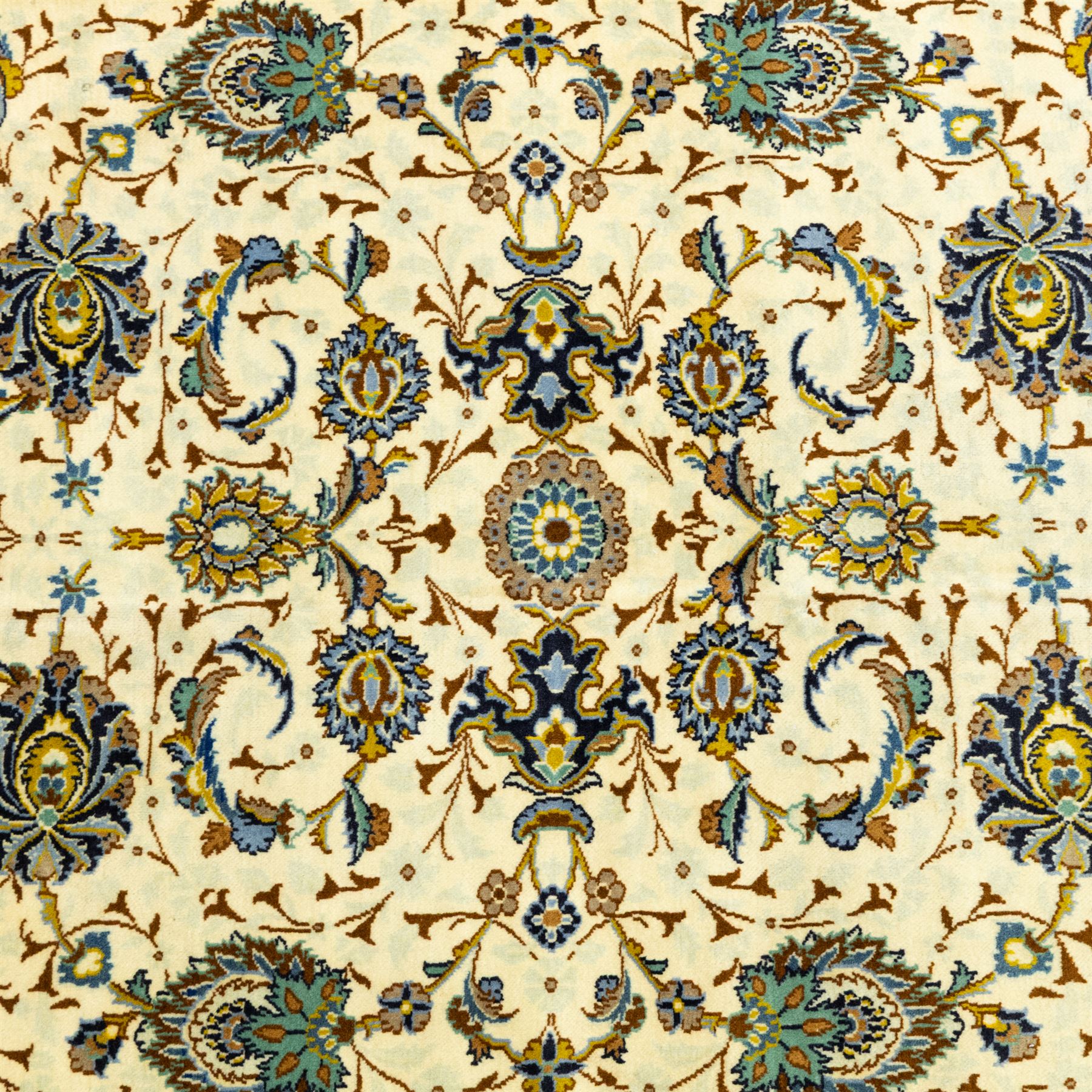 Central Persian Kashan hand-knotted carpet, ivory ground, with an all-over floral design of palmettes, scrolling vines and flowerheads in blue, ochre and beige tones, enclosed by a sage green border with repeating floral sprays and leafy scrolls, flanked by narrow guard stripes, with cotton fringes