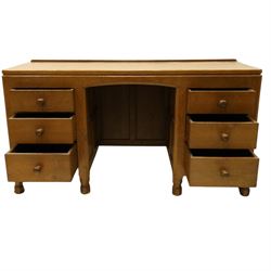 Mouseman - adzed oak kneehole dressing table or desk, the rectangular adzed top with raised back and canted corners, over an arched recessed kneehole flanked by three graduating drawers to each side with turned knob handles, raised on octagonal feet, with carved mouse signature, by the workshop of Robert Thompson of Kilburn