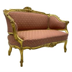 20th century French design hardwood framed giltwood settee, moulded cresting rail carved with central shell motif and extending scrolled foliage, upholstered in pink fabric decorated with repeating pattern, on cabriole supports with scroll carved terminals 