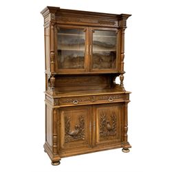 Late 19th century oak buffet cabinet, projecting moulded cornice above raised glazed cabinet with acanthus leaf and vertical fluted frieze supported by two turned columns, panelled back and moulded rectangular canted top, two drawers above cupboard enclosed by fielded panelled doors mounted with carved duck and pheasant figures in naturalist settings, flanked by two turned and fluted pilasters, moulded base with turned squat bun feet