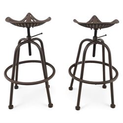 Industrial design pair of cast metal 'tractor seat' revolving bar stools, each with pierced tractor seat shaped top from the early 20th century, raised upon tubular steel supports with circular footrests (Height adjustable from 77cm - 93cm)