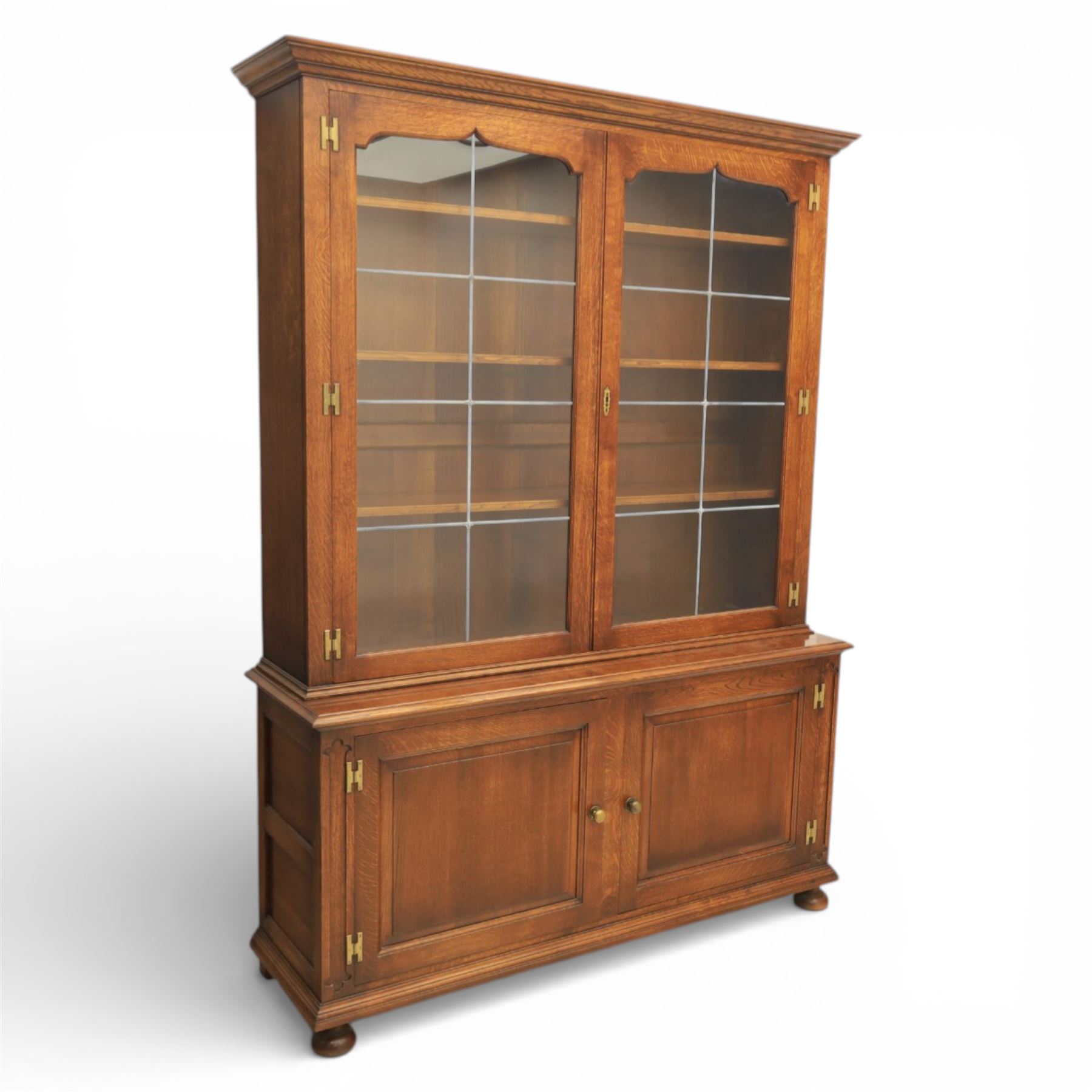 Late 20th century oak bookcase on cupboard, with moulded cornice above pair of astragal glazed doors with shaped inner frames enclosing adjustable shelves, the base with moulded top above two fielded panel cupboard doors with brass handles, upon compressed bun front feet 