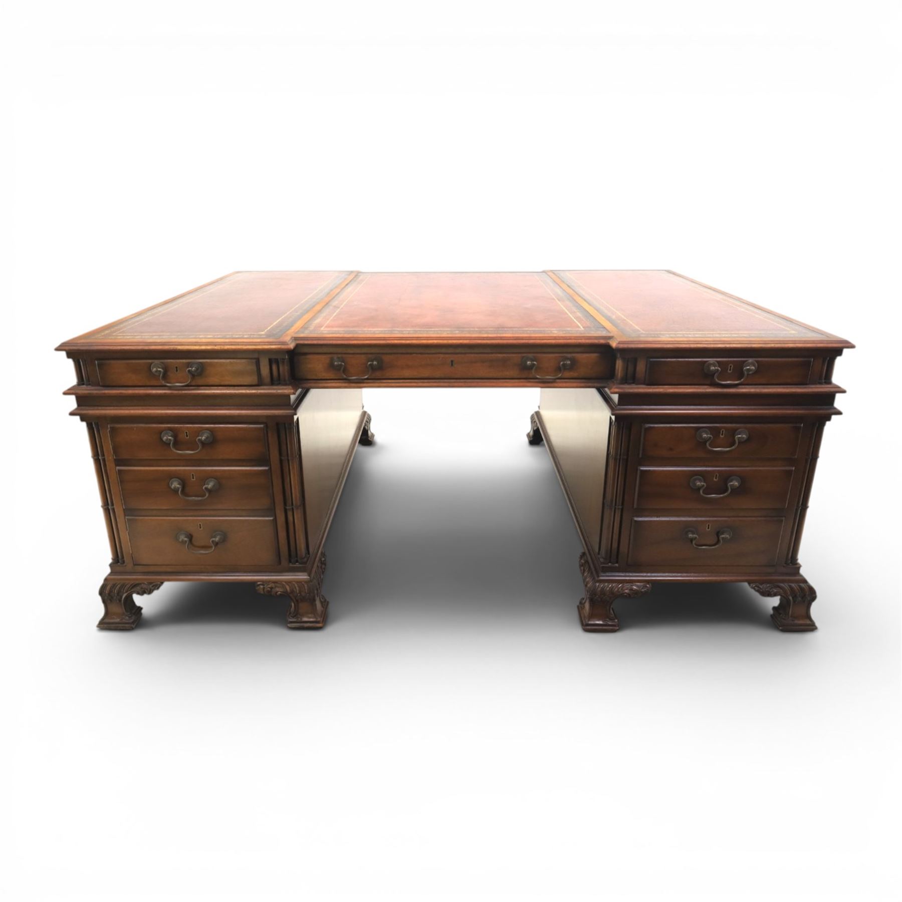 George III style large mahogany reverse breakfront partners desk, red tooled leather writing surfaces crossbanded and moulded edges, flanked by ring-turned cluster columns three frieze drawers with brass swan neck handles, raised on large pedestals with faux drawer fronted cupboard and three graduated drawers, supported on carved ogee feet decorated with C-scrolled and acanthus leaves
