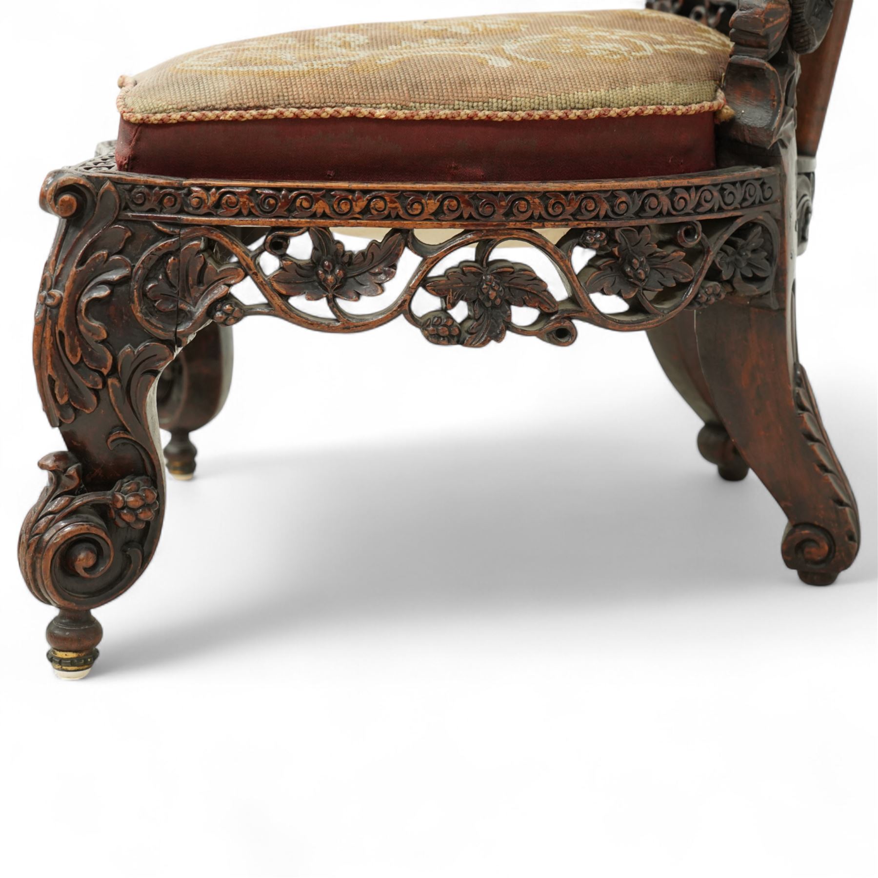Late 19th century Anglo-Indian carved hardwood nursing chair, cartouche-shaped back, pierced fruit vine carved frame, gros-point tapestry upholstered seat, on carved scroll legs 