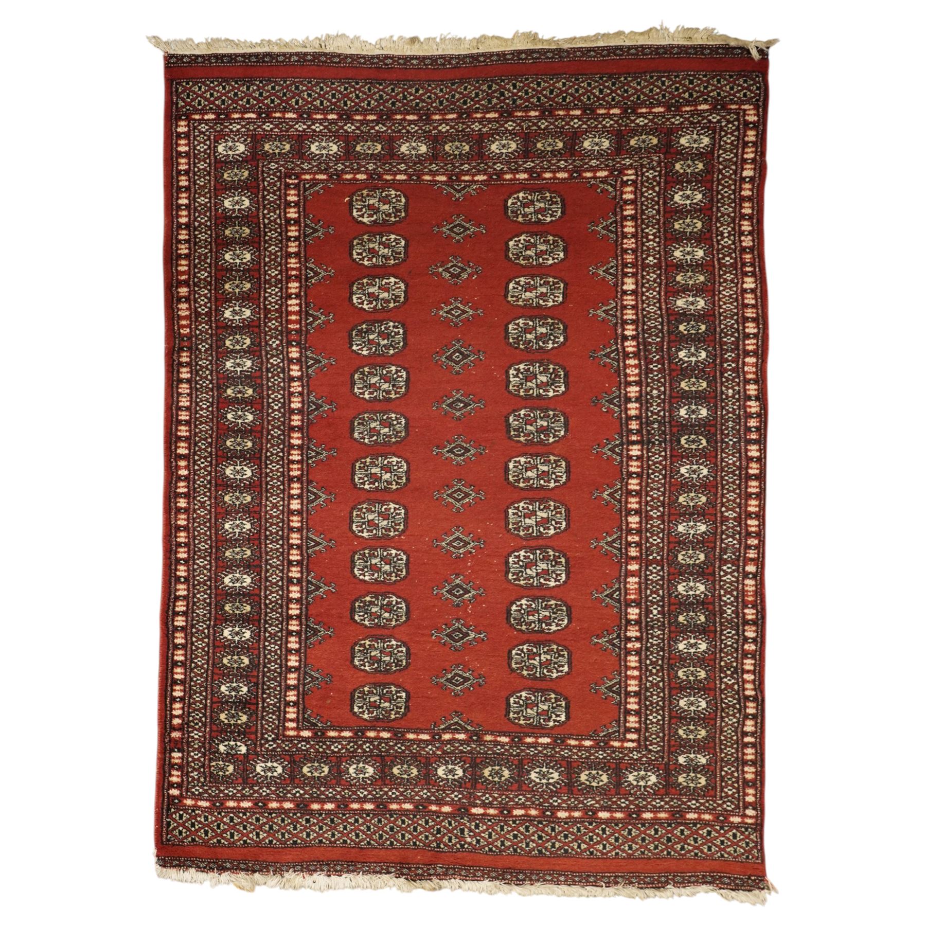 Turkoman hand-knotted rug, madder red ground with two rows of repeating octagonal guls interspersed with geometric motifs, enclosed by multiple geometric and stylised floral borders, with fringed ends