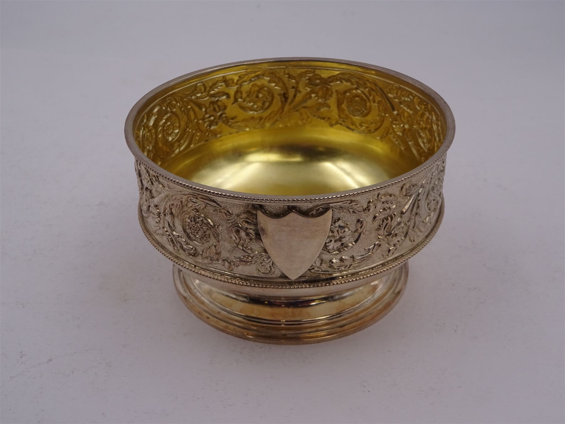 Victorian silver bowl, with embossed floral decoration and beaded rim, gilt interior and two applied shield cartouches, upon stepped circular foot, with a silver apostle spoon, with gilt bowl, both hallmarked George Unite, Birmingham 1883, bowl H5.5cm, within fitted tooled leather, silk lined case