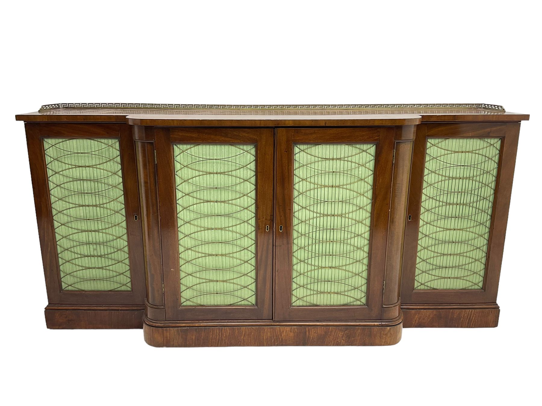 19th century mahogany break-front sideboard, raised brass gallery back with Greek key design, fitted with four cupboard doors, their pleated green fabric overlain with gilt metal grilles, lower moulded edge over plinth base