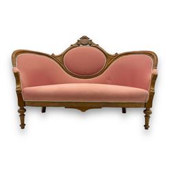 Late Victorian walnut framed double spoon back sofa, shaped crest rail with central carved medallion over curved back with pink upholstery, scrolling arms with additional carvings, on turned supports