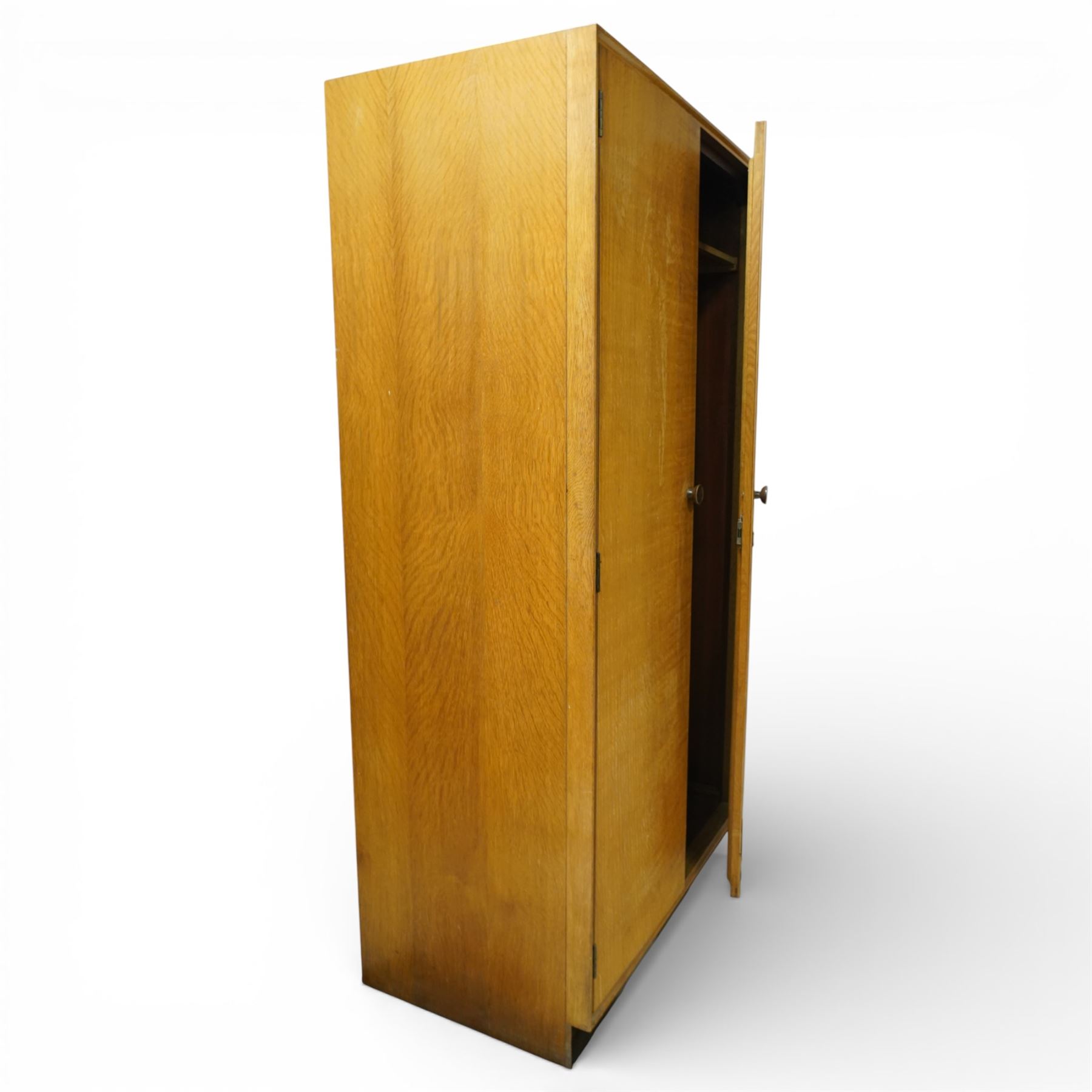 Mid 20th century oak veneered wardrobe, the plain rectangular top above a pair of hinged doors fitted with circular handles, opening to reveal a hanging rail and upper shelf, one door with inset mirror, the whole raised on a plinth base