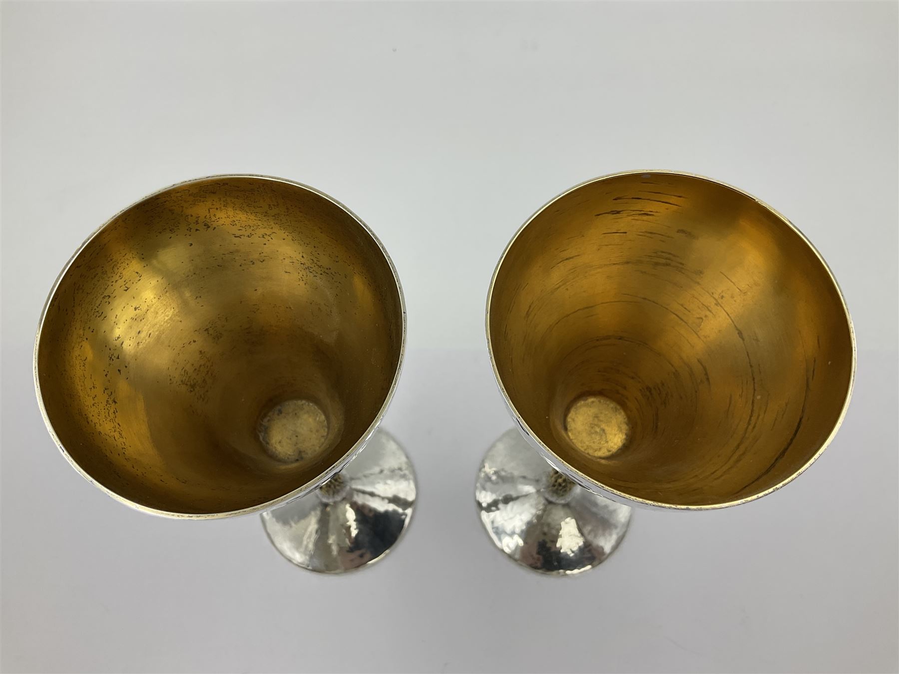 Pair of modern silver goblets by Stuart Devlin, the tapering cylindrical bowls each with spot hammered decoration and gilt interiors, the parcel gilt stems with signature textured detailing and six graduating knops, upon conforming spreading circular foot, hallmarked Stuart Devlin, London 1976, H17.7cm