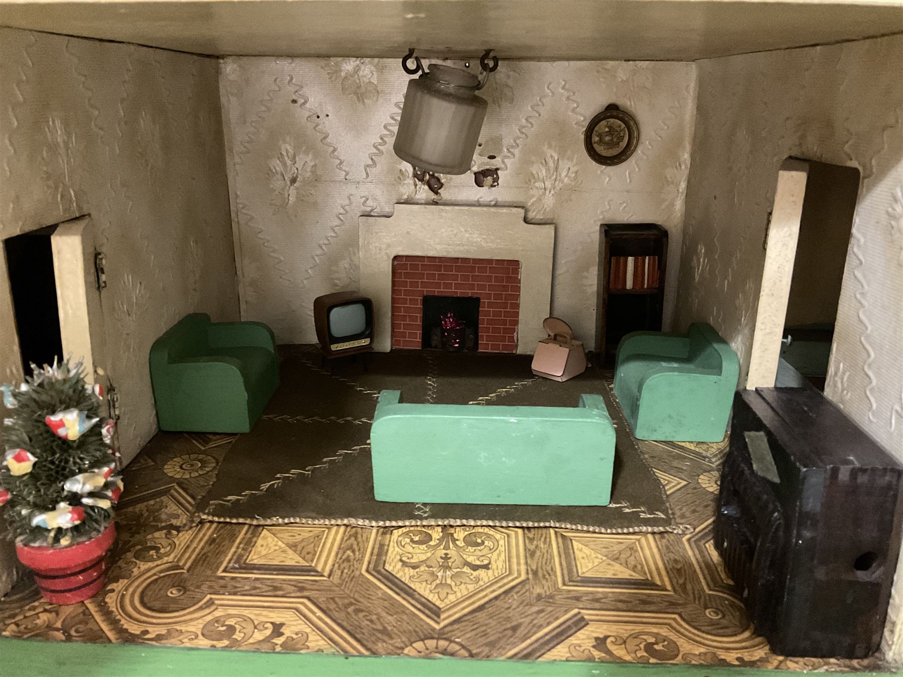 Large Tri-ang No.93 doll`s house in the 'Stockbroker's Range' c1935; two-storey double-fronted Tudor design, half timbered gables, two-storey bay windows, cream and mock shrubbery to front, opening metal framed windows with green shutters, red simulated tiled roof with chimney, integral garage with opening doors, front elevation has four hinged doors opening to reveal two bedrooms with fire places, living room, bathroom and kitchen with built in dresser and sink, entrance hall and staircase, side entrance with porch and seat and sun dial over on chimney stack; some wiring for electrical lighting; metal Tri-ang Toys disc verso; comprehensively furnished H66cm L117cm D43cm