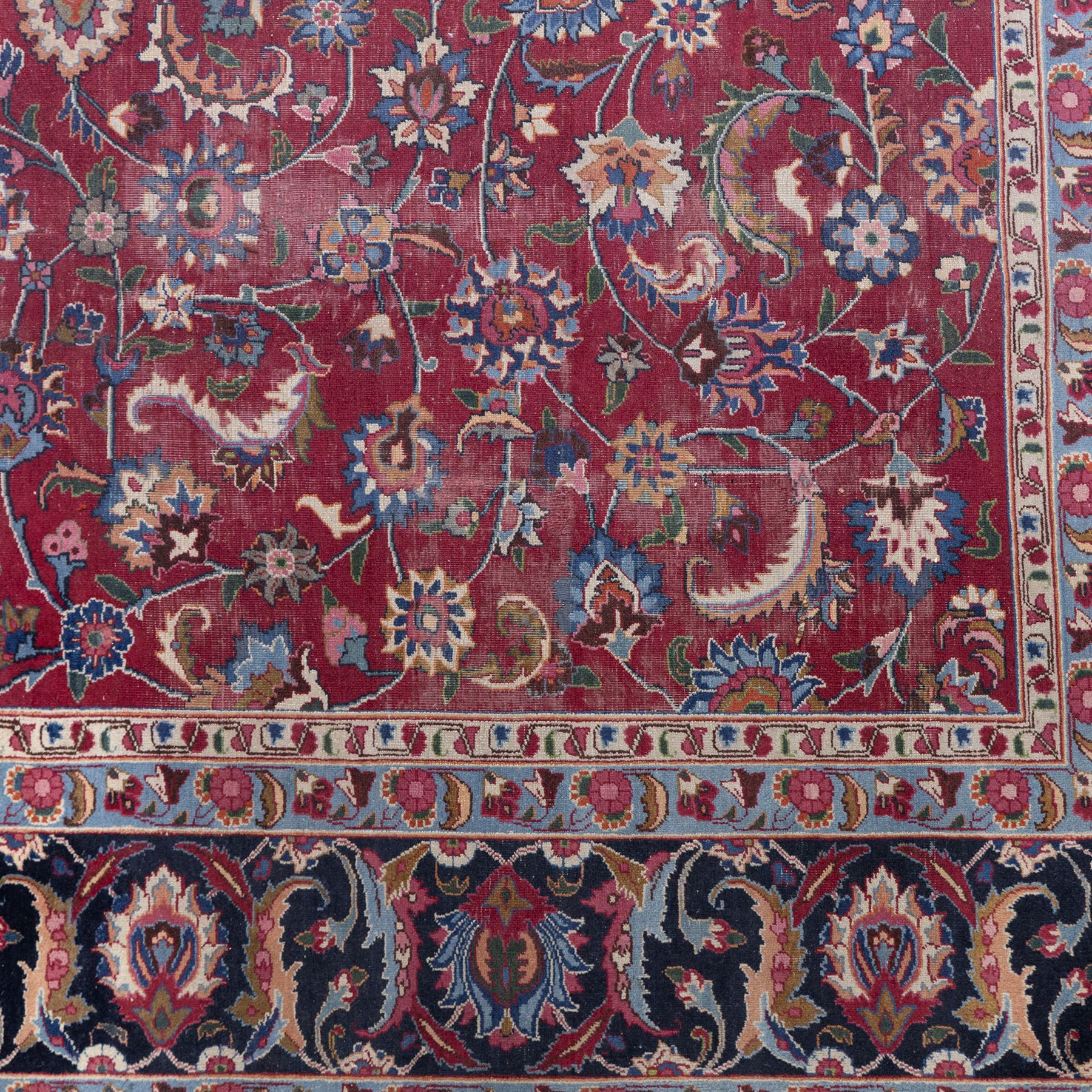 Persian Mashad design wool carpet, the red ground with dense scrolling floral and foliate decoration, within dark blue main border decorated with repeating palmettes and shaped leaves