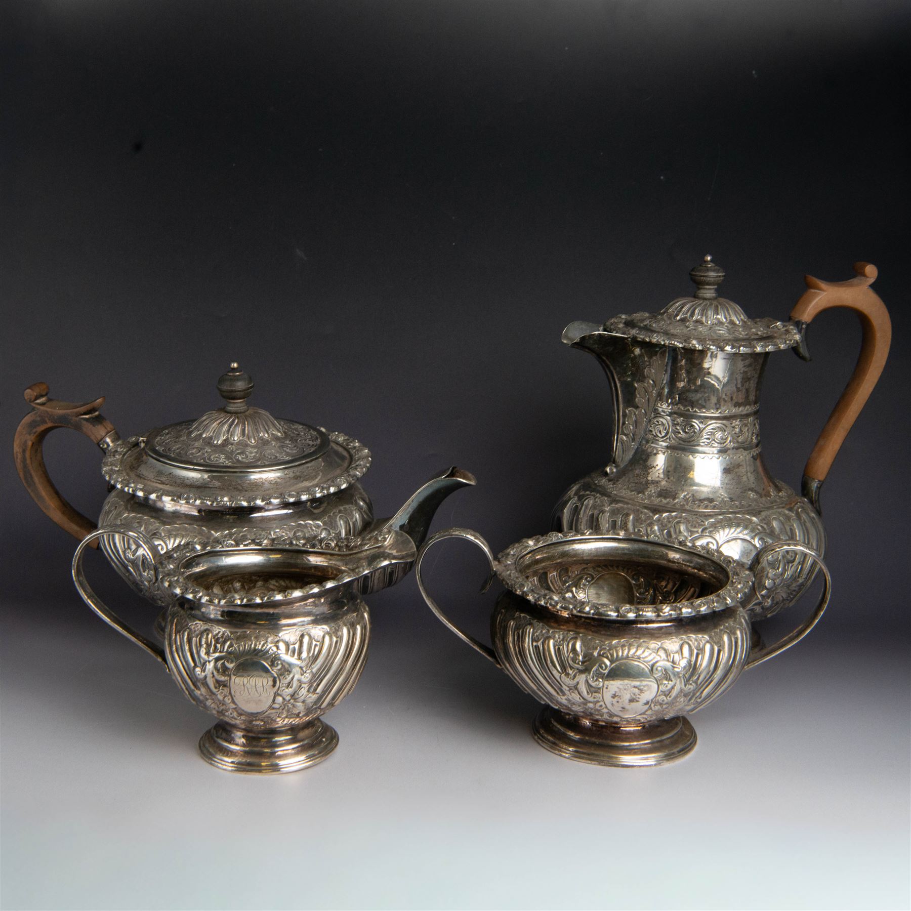 Victorian silver four piece tea service, comprising hot water pot, teapot, milk jug and sugar bowl, of circular part fluted bellied form, with embossed and engraved floral decoration, engraved with initials to body, the teapot and hot water pot with wooden handles and finials, hallmarked Z Barraclough & Sons, Sheffield 1898