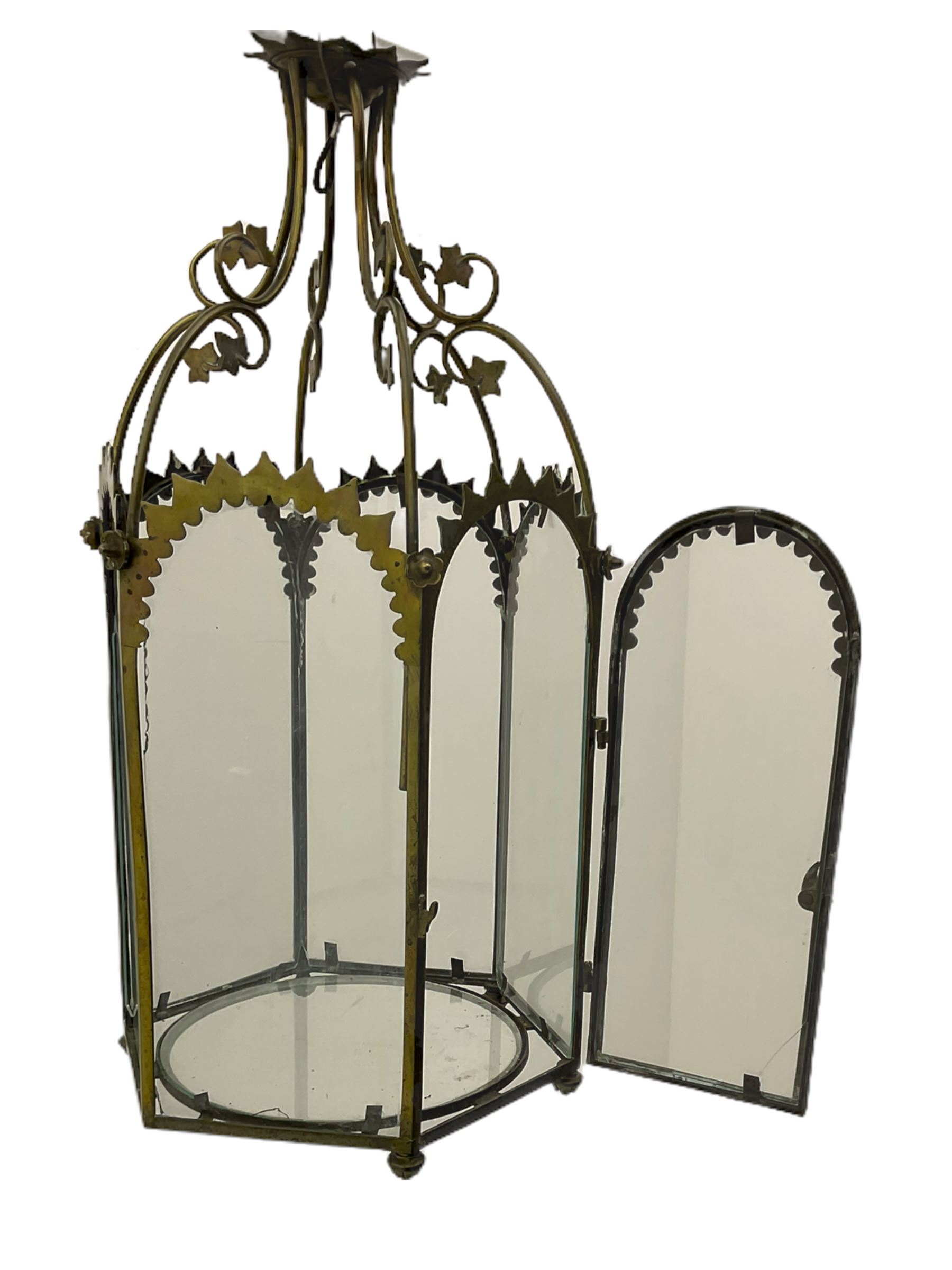 19th century brass and clear glass hexagonal hall lantern, with scrolling wire work open domed top over six arched panels, including a hinged door, the base enclosed with a circular glass panel on turned feet, H64cm