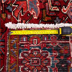 North West Persian Heriz hand-knotted carpet, brick red field, with large central angular star medallion with stepped outlines, surrounded by geometric floral devices and stylized rosettes, with corresponding corner spandrels, enclosed by a bold geometric main border with multiple guard stripes, with cotton fringe ends 