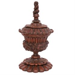 Carved wooden urn. decorated in relief with carved faces within foliage, with a Satyr finial, H25cm 