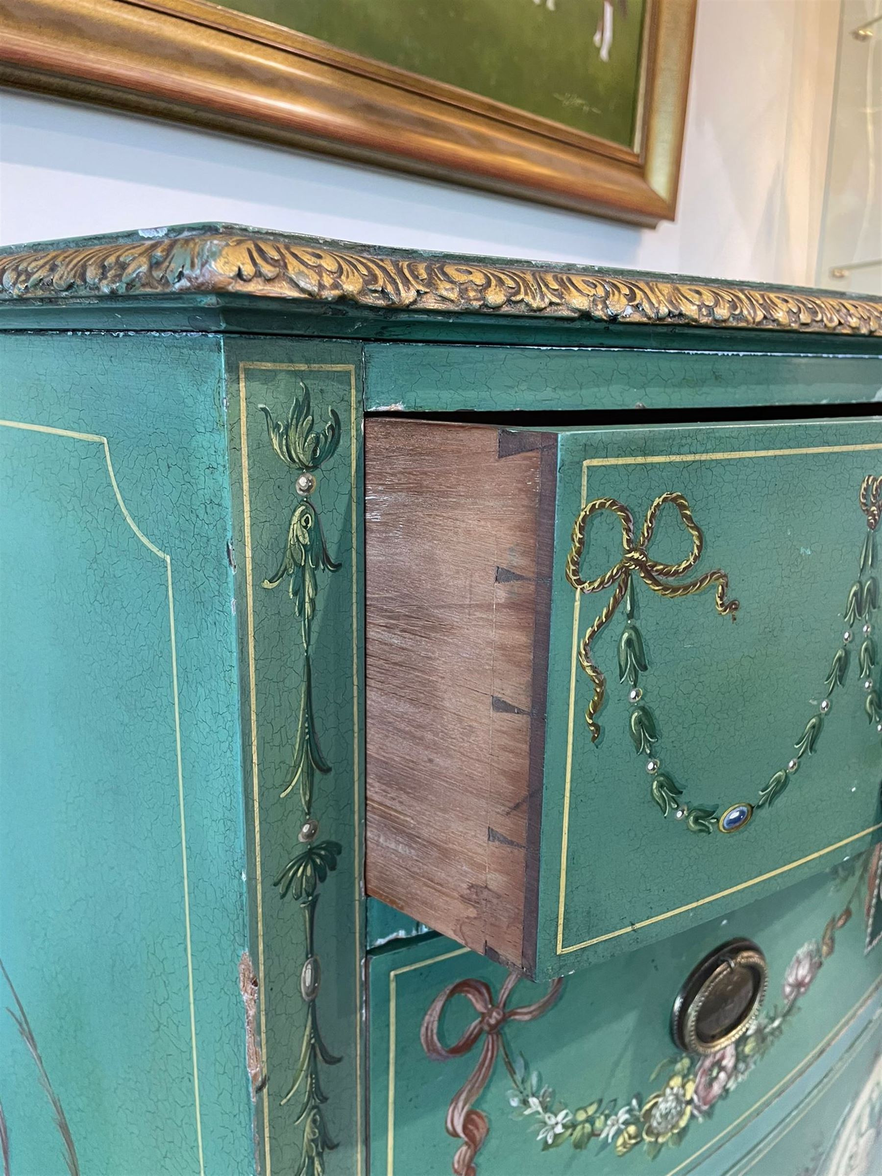 Edwardian Adam Revival green-painted and parcel gilt bowfront chest, moulded and foliate carved top painted with trailing floral band, fitted with four drawers decorated with trailing floral festoons, ribbon ties and urns, oval handle plates with engraved decoration and bead cast handles, on turned supports decorated with acanthus leaves and draped festoons 