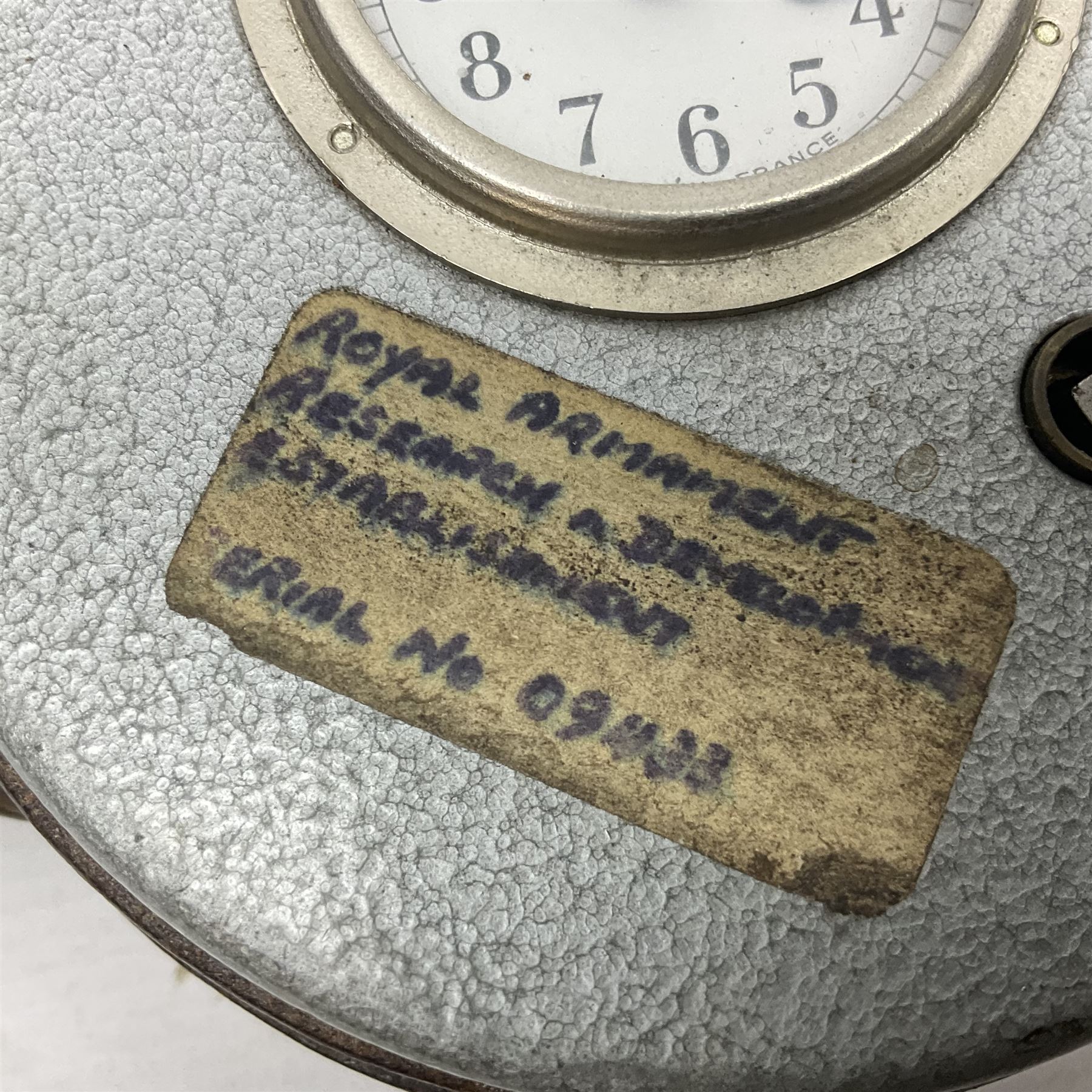 Metal cased drum shaped travelling clock with grey hammered finish, French clockwork movement and stitched leather outer case with shoulder strap; bears manuscript label 'Royal Armament Research and Development Establishment - serial no.09433' D13cm overall