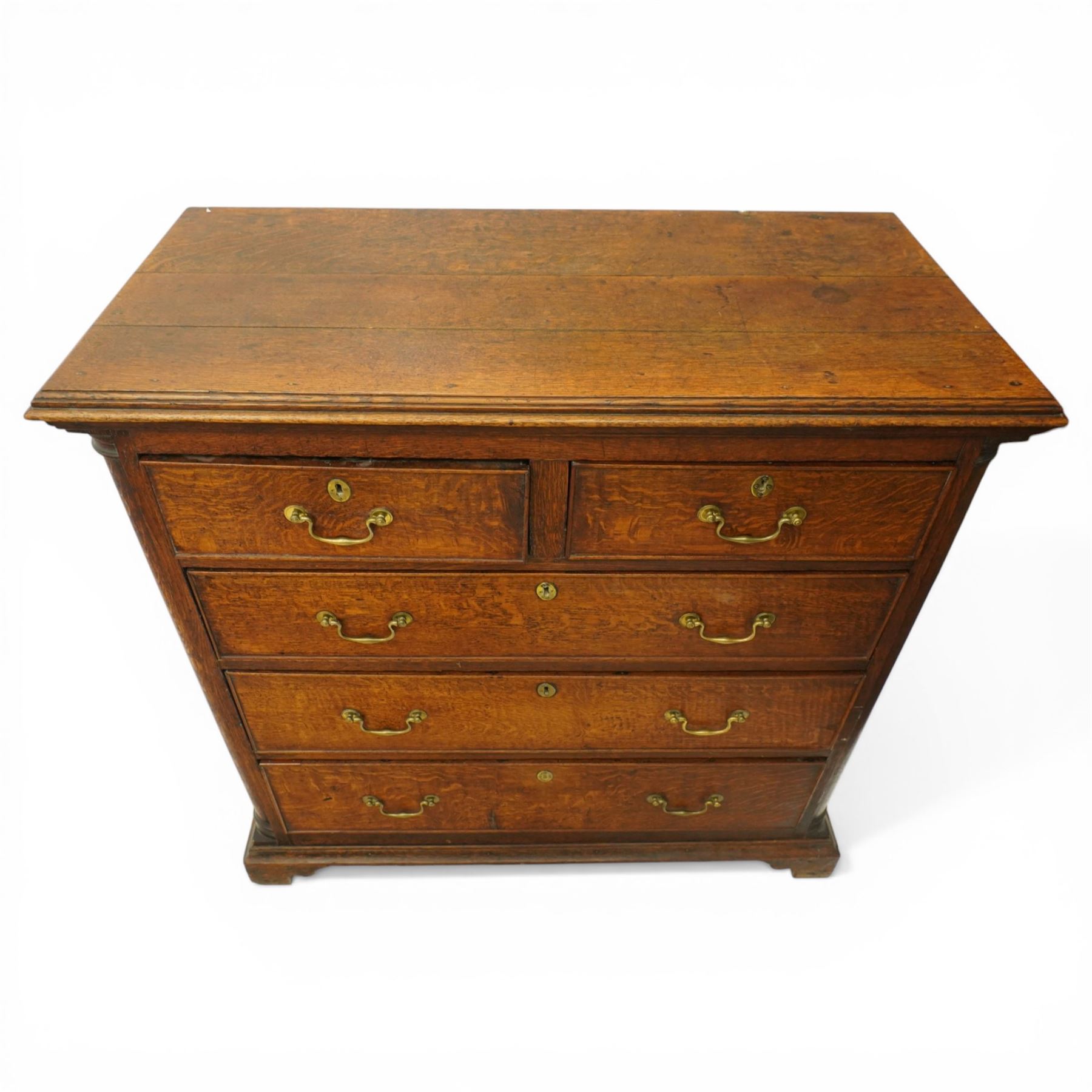 Georgian oak chest of drawers, fitted with two short over three long drawers, with brass swing handles and escutcheons, flanked by quarter turned pilasters, raised on shaped bracket feet