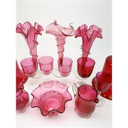 Three Victorian cranberry glass trumpet vases, each with spiralling frilled or crimped decoration, largest H24cm, together with two large Victorian cranberry glass bells, with clear glass handles, H32cm, and a selection of other cranberry glass, comprising bowl, two jugs, and five drinking glasses. (Qty). 