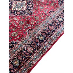 Central Persian Kashan carpet, red ground field with blue medallion and spandrels, decorated all-over with trailing foliate and stylised plant motifs, scrolling design border with guards