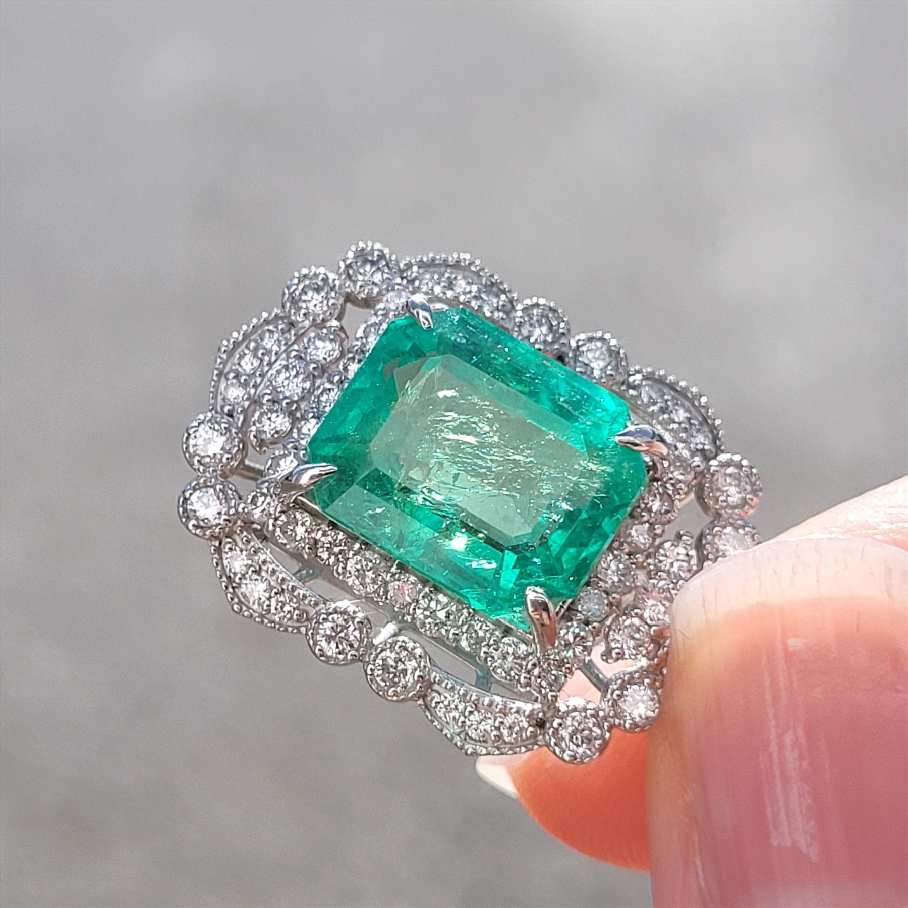 Platinum Colombian emerald and diamond pendant necklace, single octagonal cut emerald of 7.38 carat, surrounded by round cut diamonds in a fancy milgrain pierced design setting, stamped Pt 950, on a trace link chain necklace, total diamond weight 1.14 carat, with GCS certificate